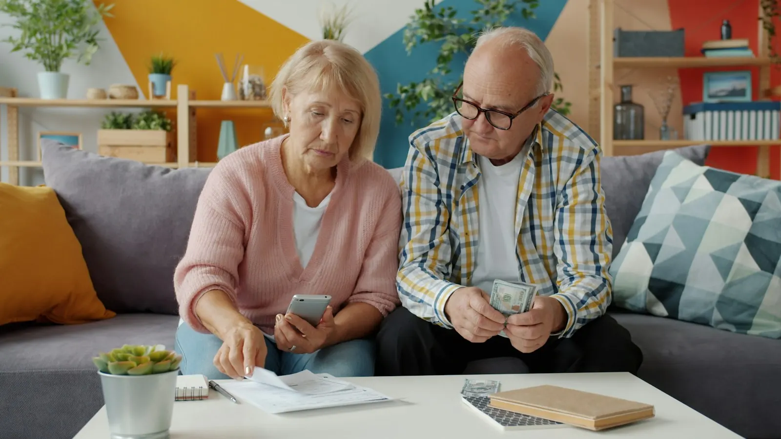 An older couple at home looking over paperwork and a phone together