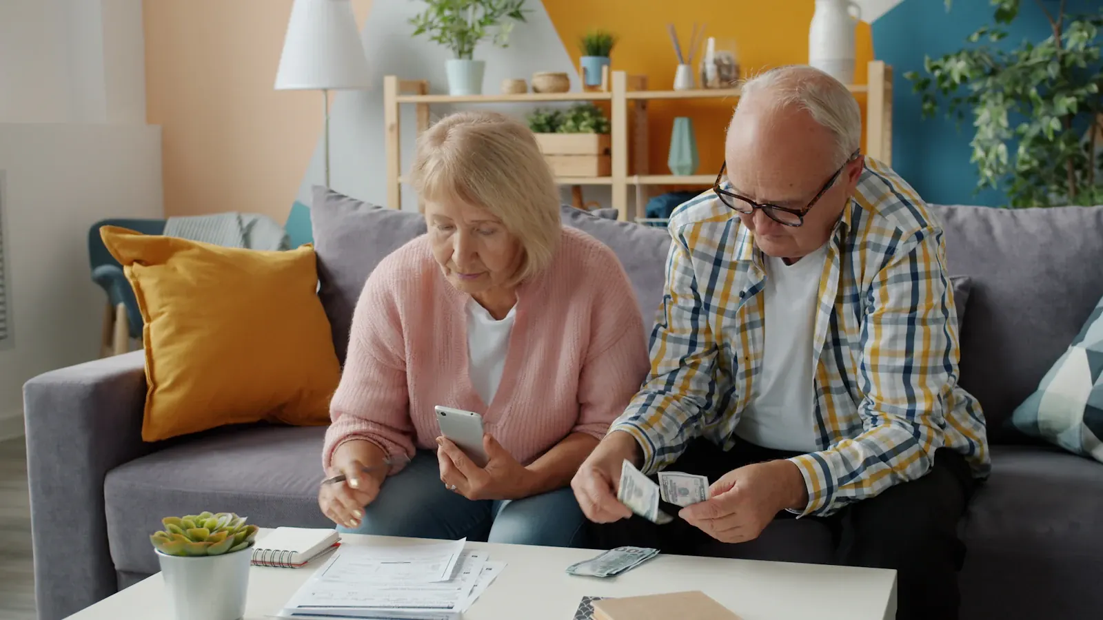 An older couple sitting together on a sofa at home, reviewing their household finances