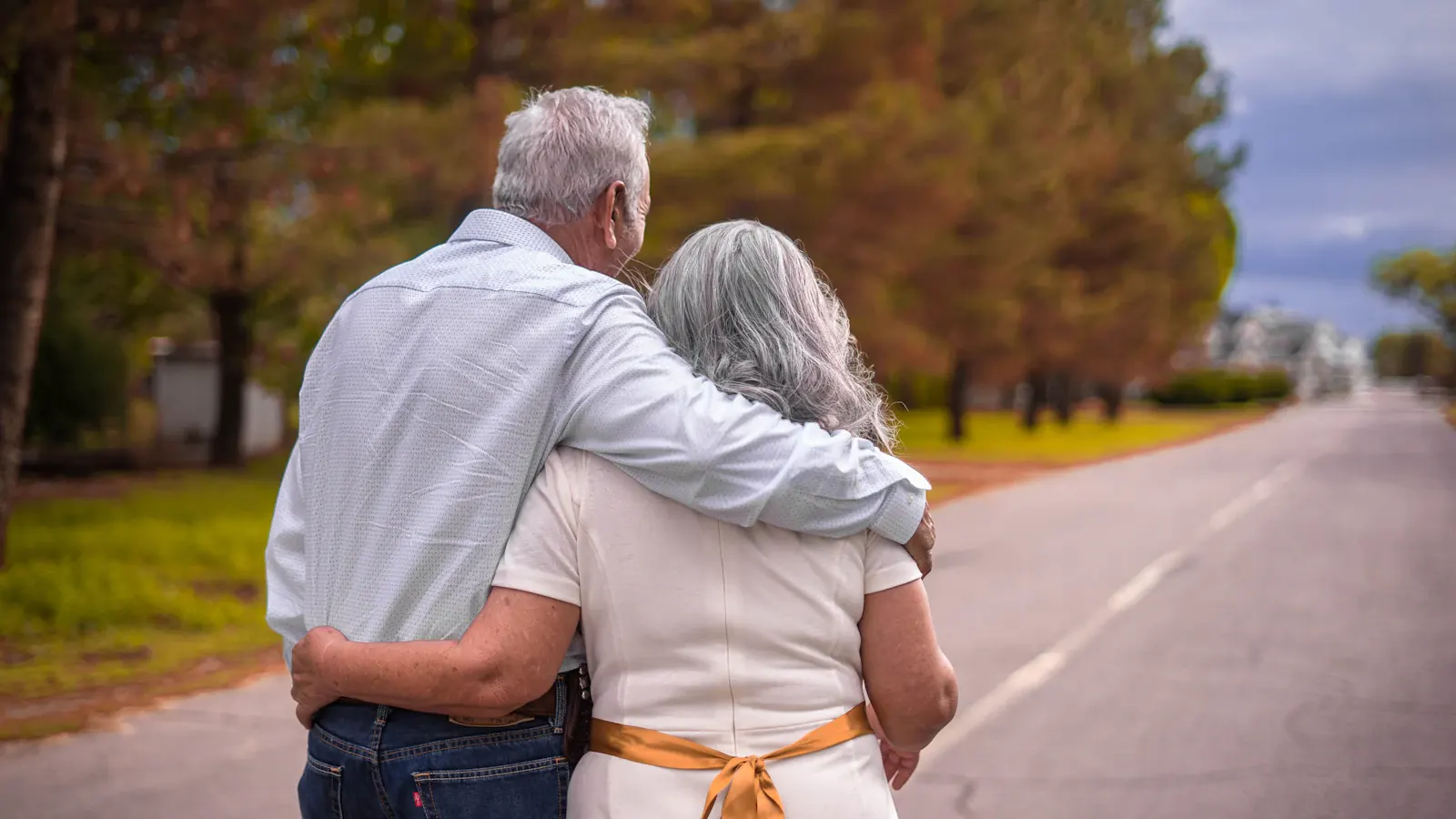An older couple walking arm in arm down a long open road