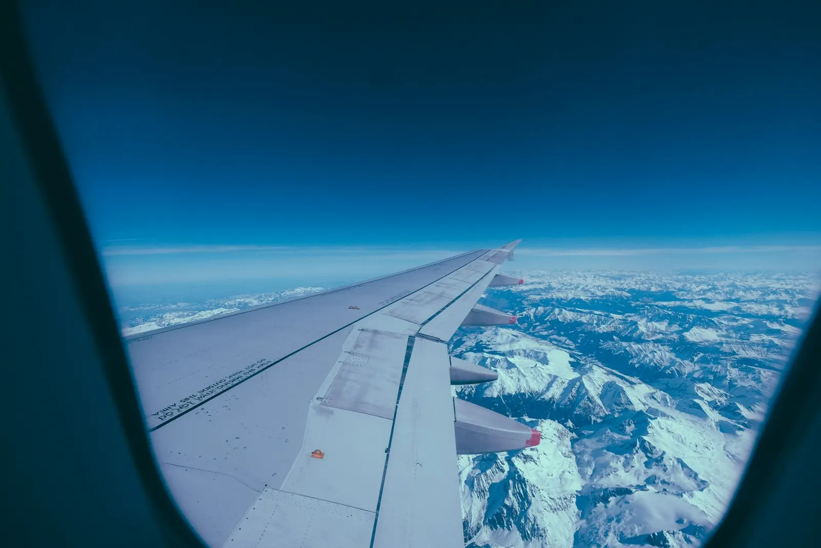 View from an airplane window of the wing above snow-covered mountains